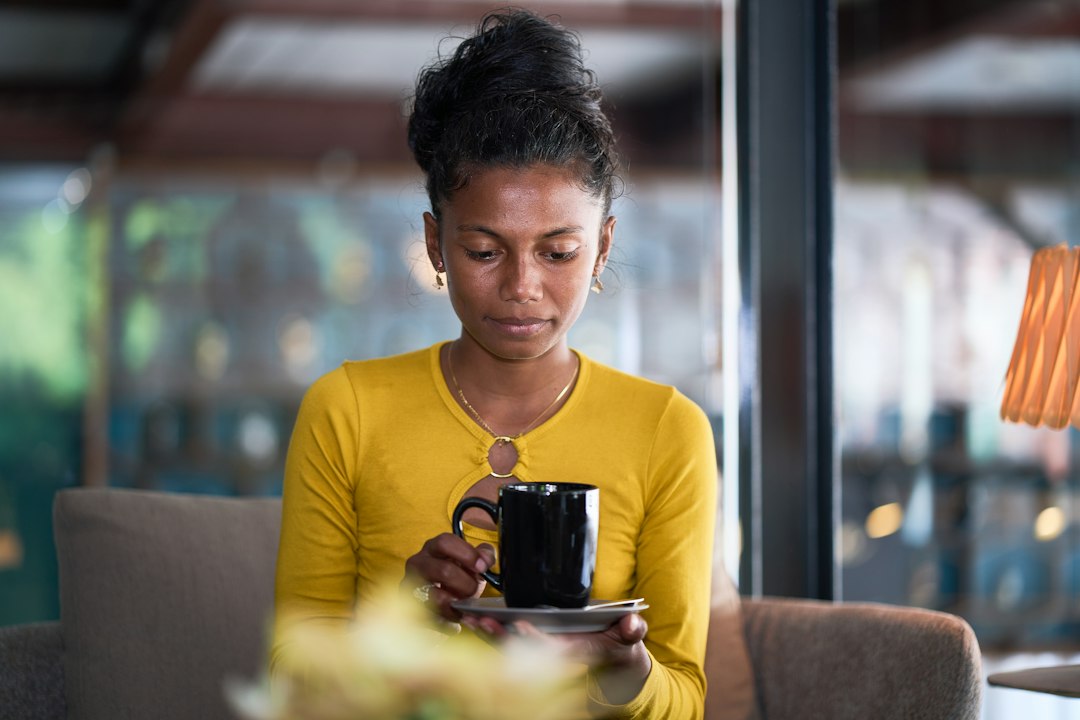 A woman in a yellow shirt mindfully observes a black mug she is holding