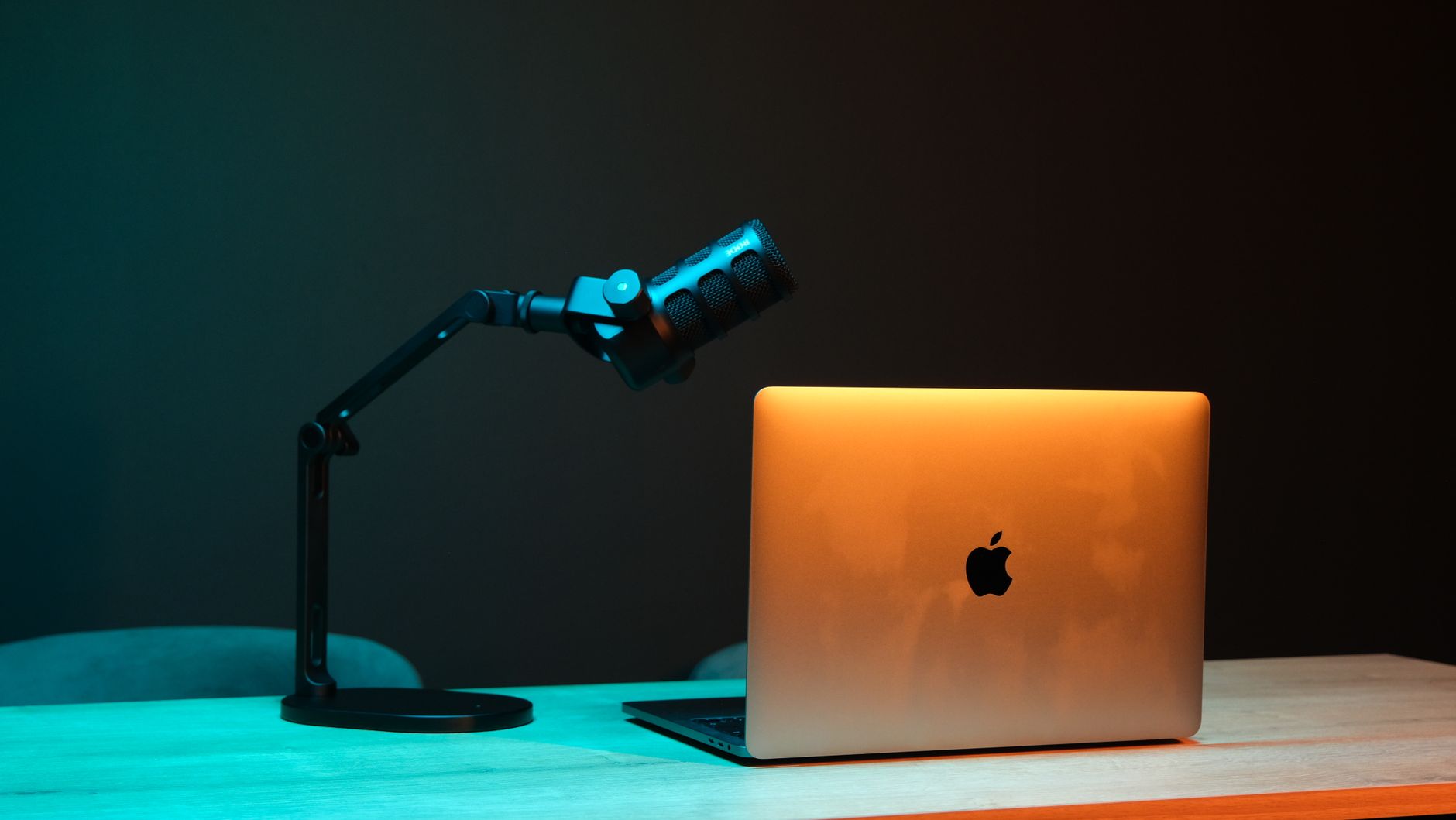 A podcast microphone on a boom arm next to an open laptop on a desk