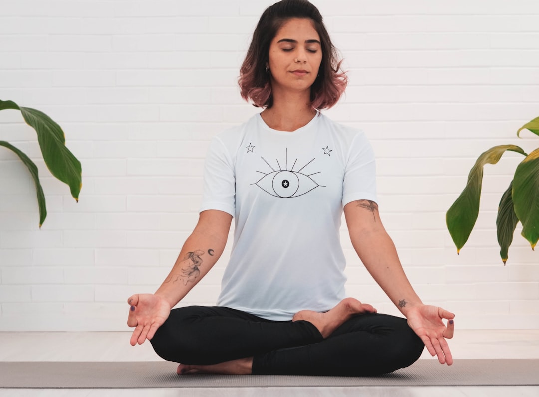 Woman meditating in lotus pose with closed eyes, surrounded by plants