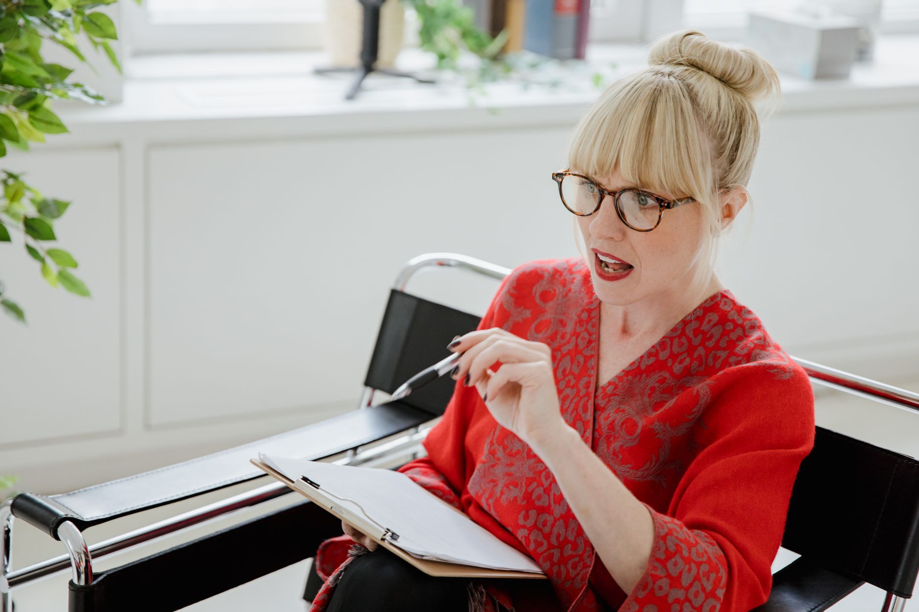 Blonde therapist with glasses holding a clipboard and pen, explaining something