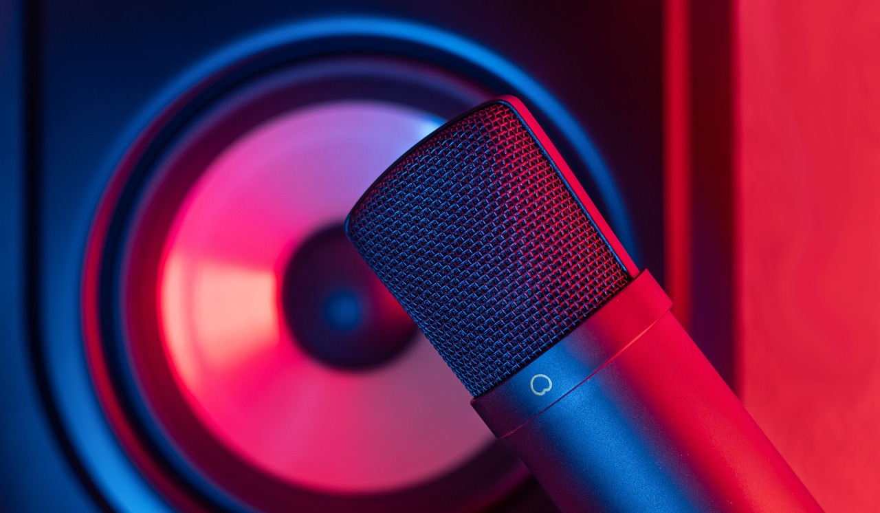 A professional condenser microphone in neon red and blue light near a speaker cone