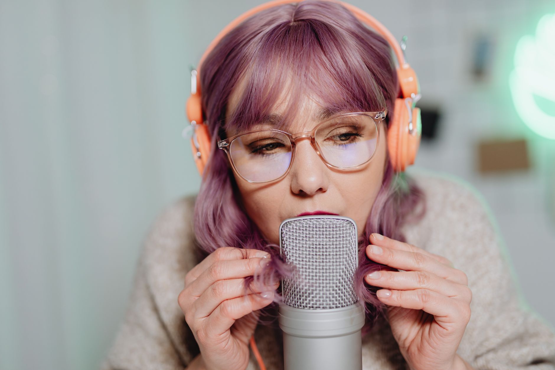 Woman with purple hair, headphones, and glasses speaking into a podcast microphone