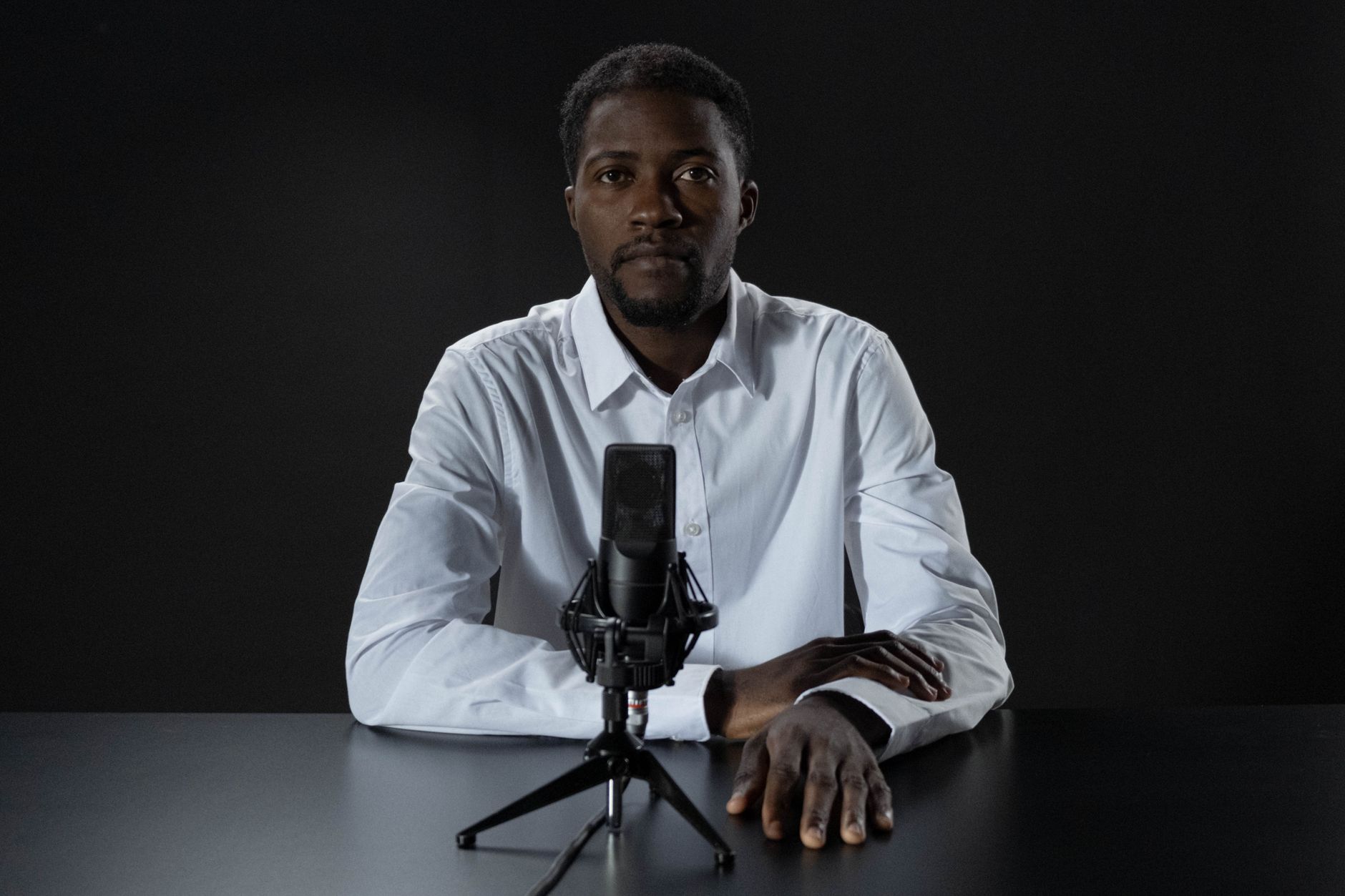 Man in a white shirt sitting at a table with a microphone for podcasting