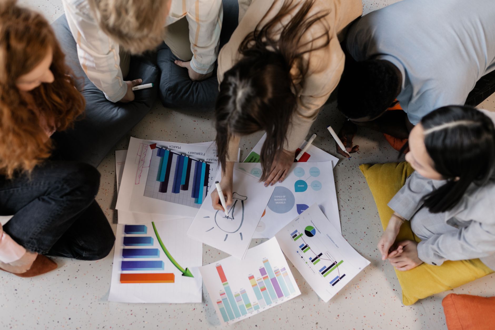 People sit on the floor in a circle reviewing printed charts and diagrams