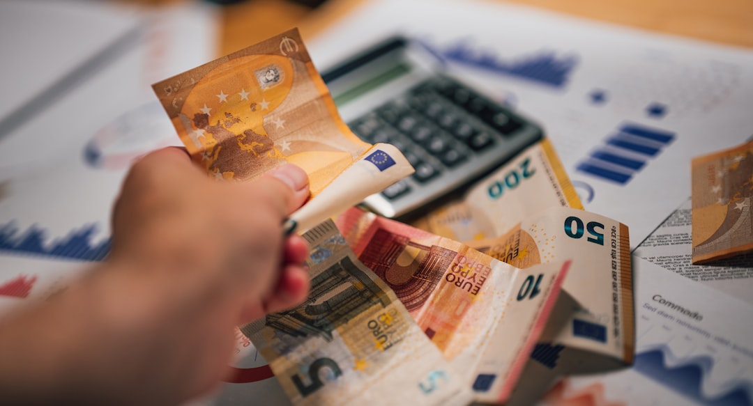 Hand holding Euro banknotes over a calculator and financial charts