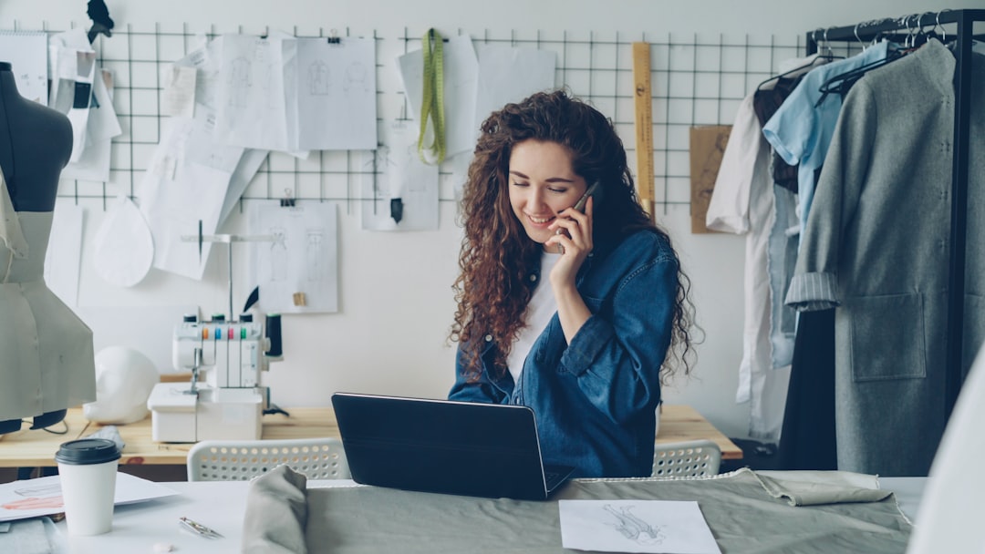 A smiling woman talks on the phone while working on a laptop in a design studio