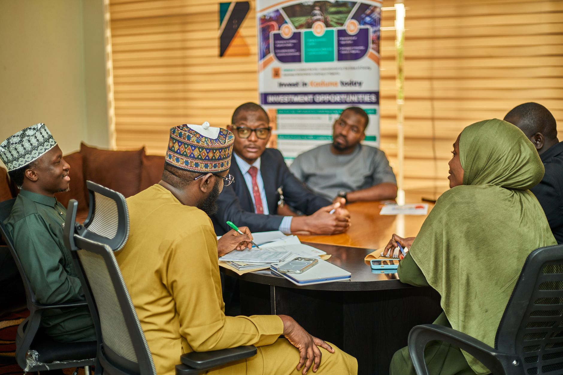 A diverse group of Nigerian people discuss land tenure opportunities around a table