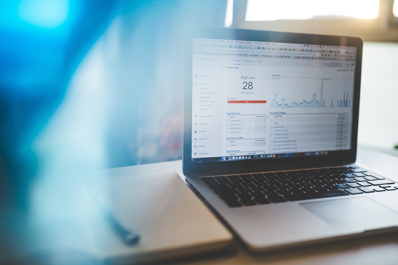 Laptop displaying Google Analytics Real-Time report with a notebook and pen nearby