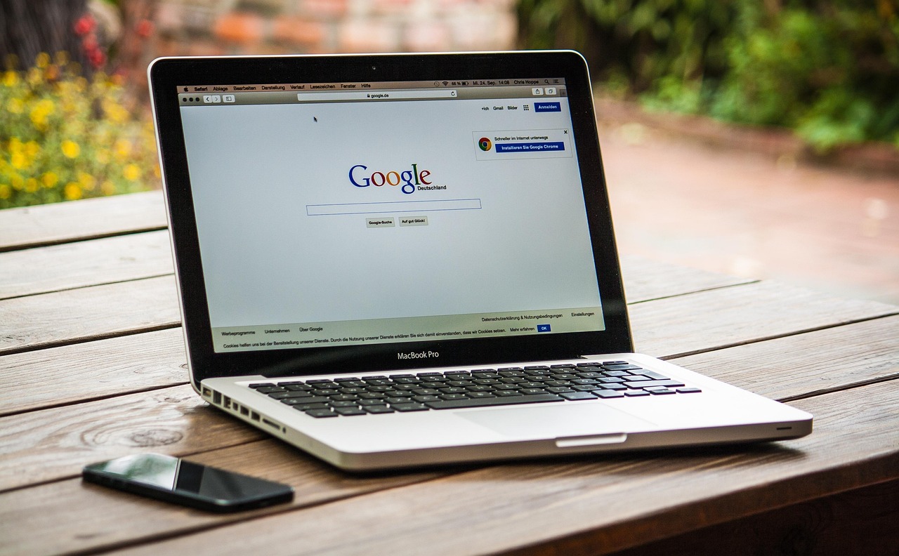 MacBook Pro displaying Google search page next to a smartphone on a wooden table