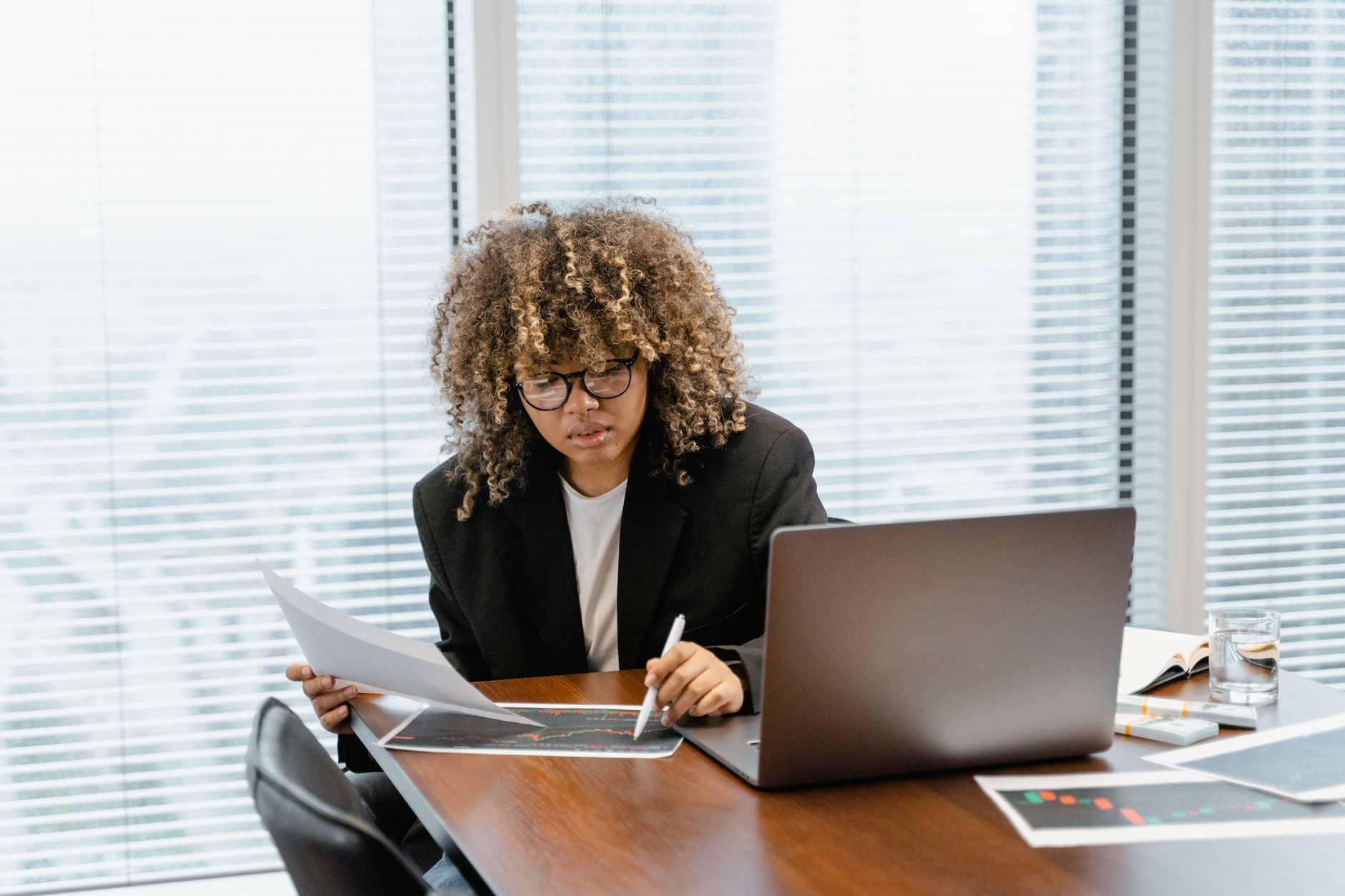 Person with curly hair analyzing charts and data on a desk with a laptop
