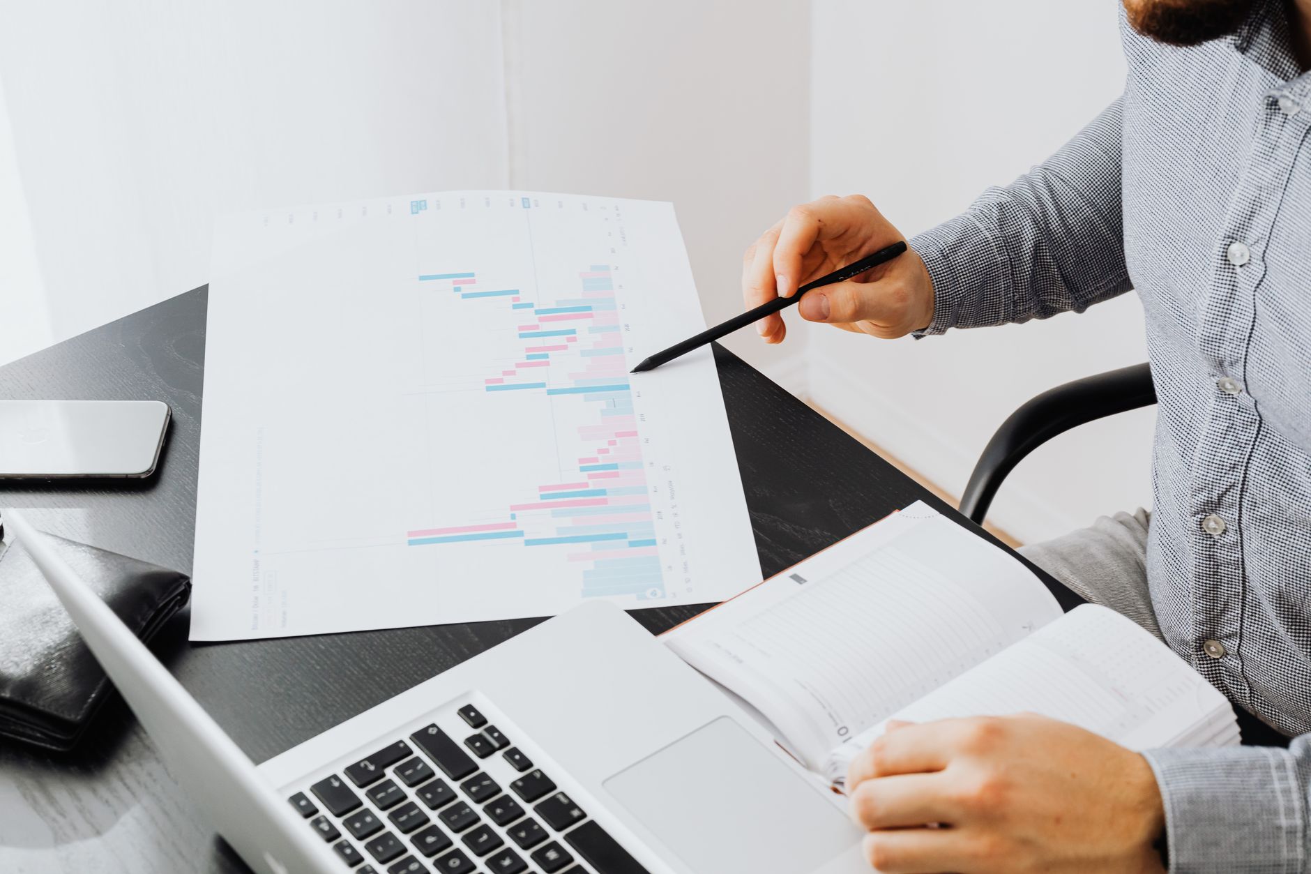 A person points a pen at a printed chart beside an open laptop