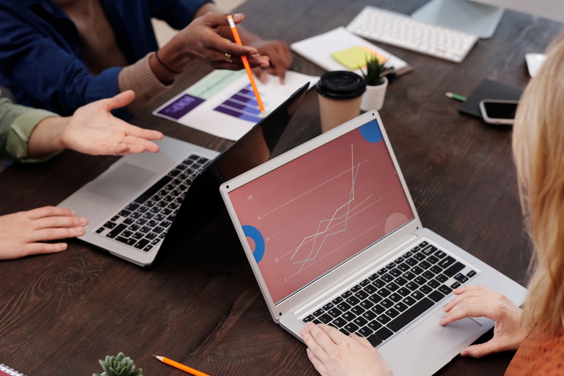 People sit around a wooden table looking at charts on laptops and paper