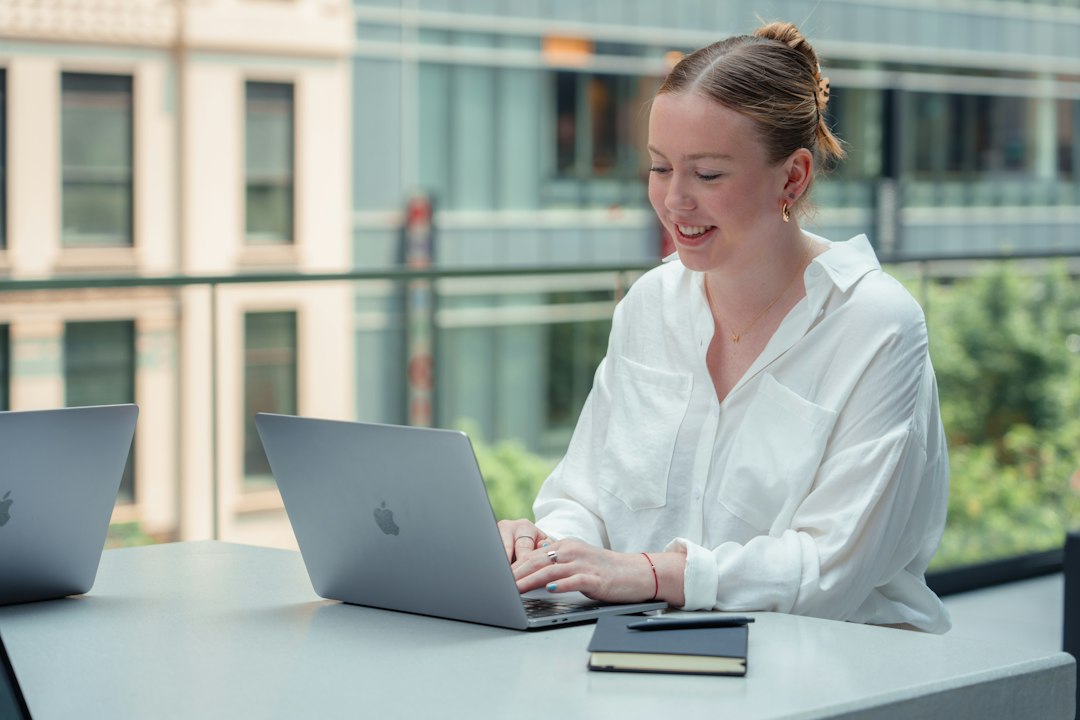 A smiling woman in a white shirt types on a laptop outdoors