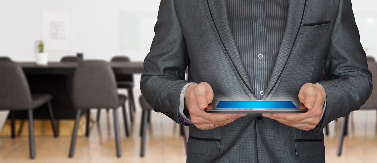 A person in a suit holds a tablet with a glowing blue interface in an office