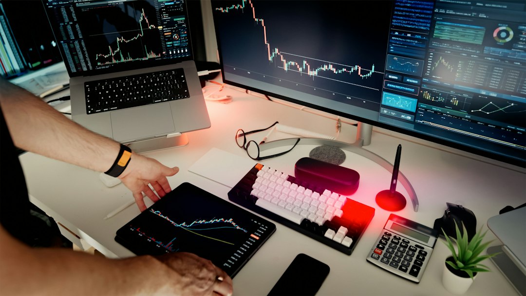 A person stands over a desk with multiple screens displaying financial graphs