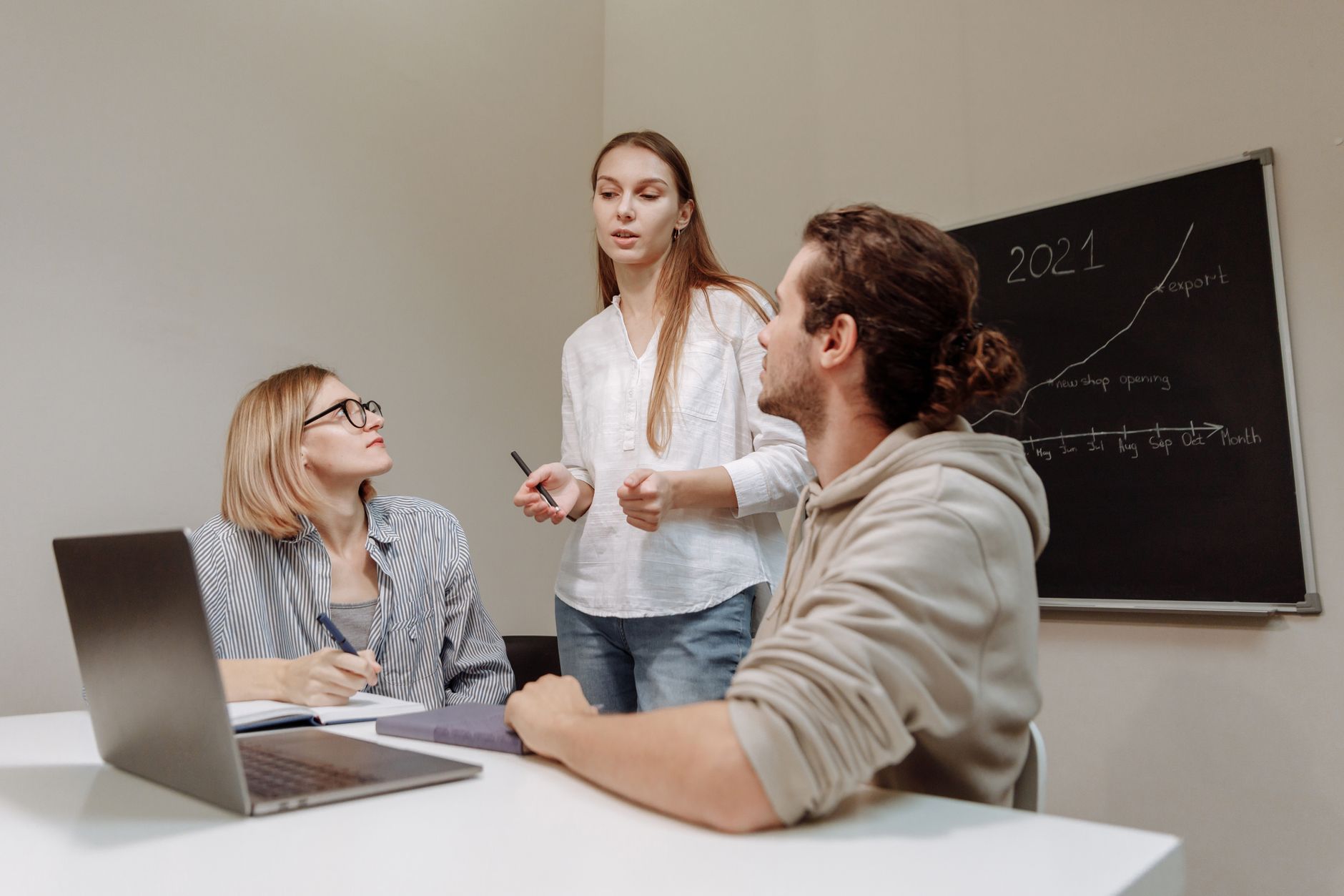 Three people discussing a startup's 2021 export growth plan with a blackboard