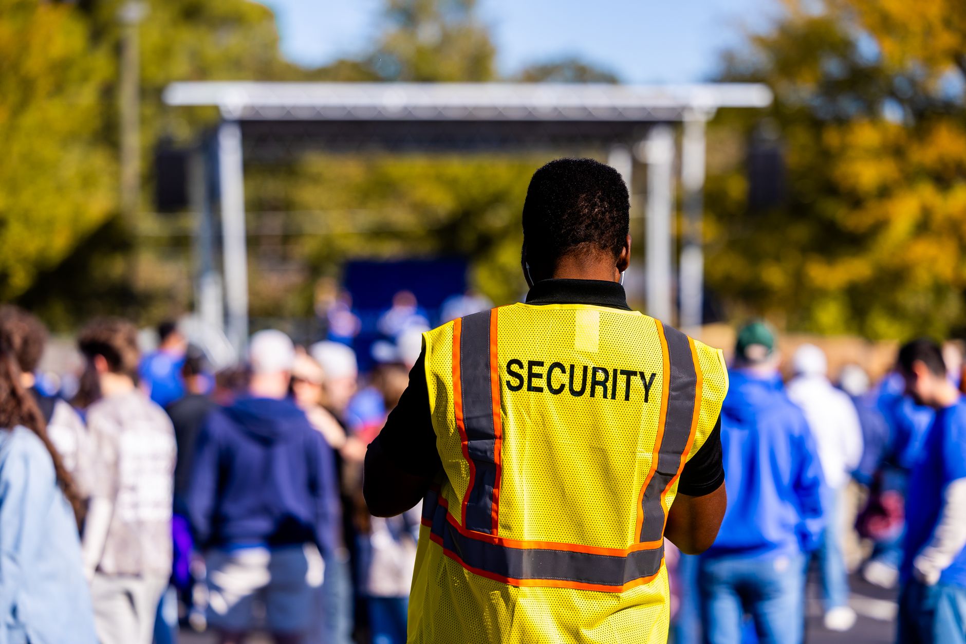 Security guard in yellow vest oversees a large crowd at an outdoor event