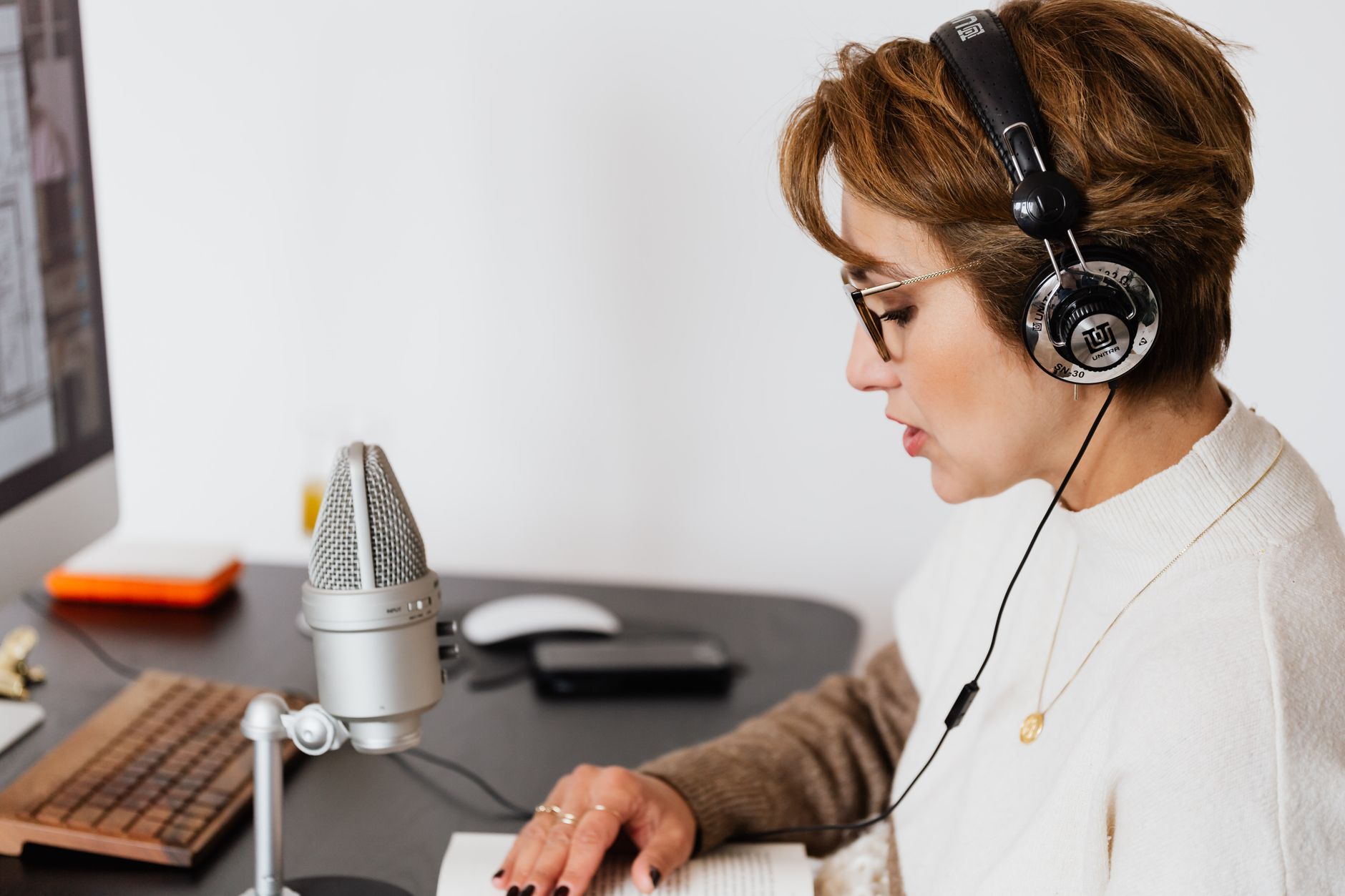 Woman wearing headphones speaking into a microphone while reading a book