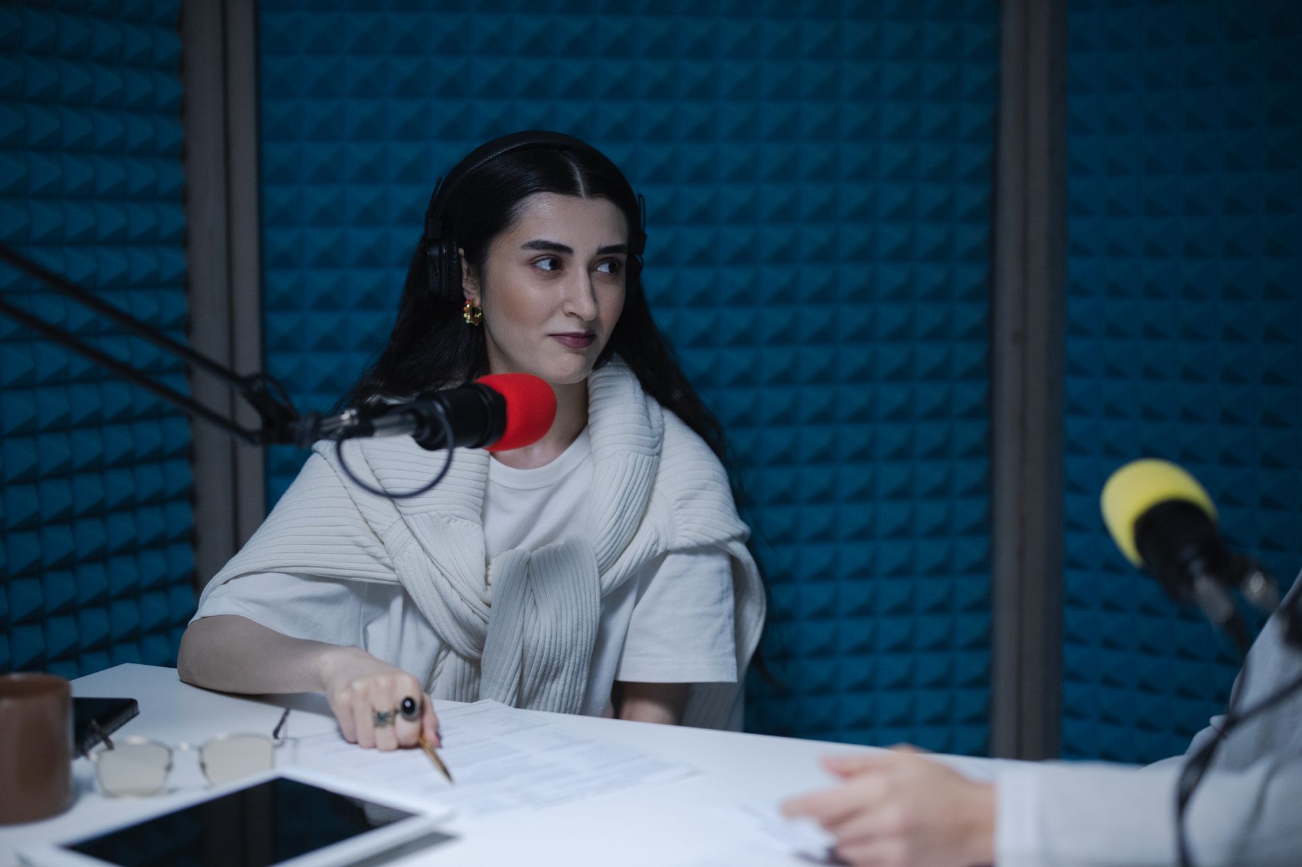 A woman wearing headphones sits before a microphone inside a recording studio