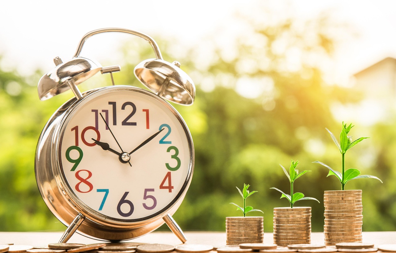 An alarm clock sits next to growing plants on stacks of coins