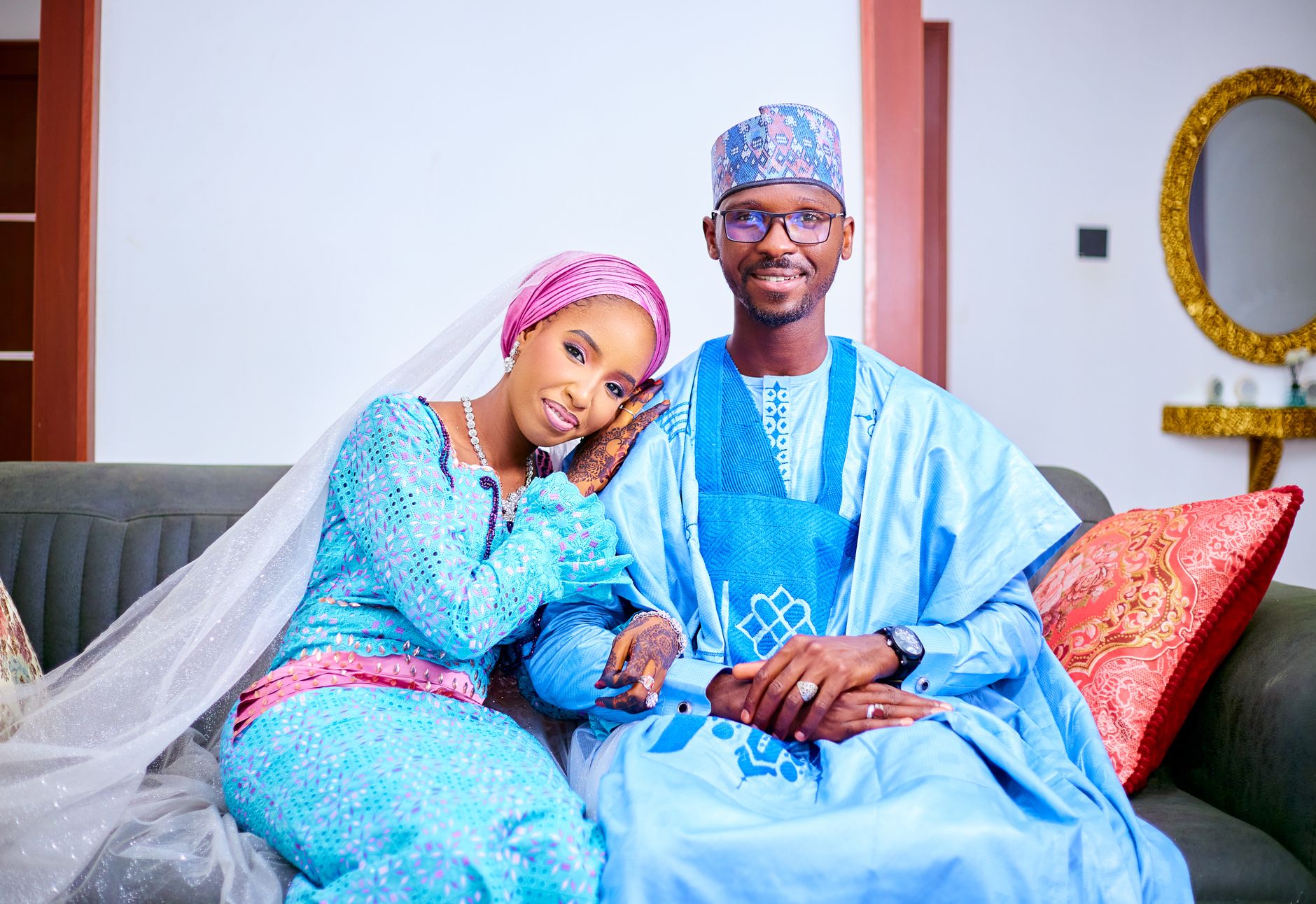 A Nigerian bride and groom in traditional attire pose together on a sofa