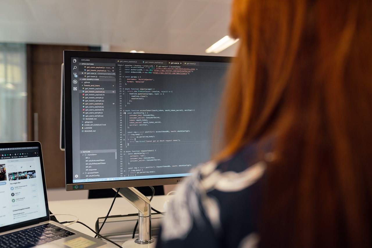 Person with red hair coding custom software on a large monitor with a laptop nearby