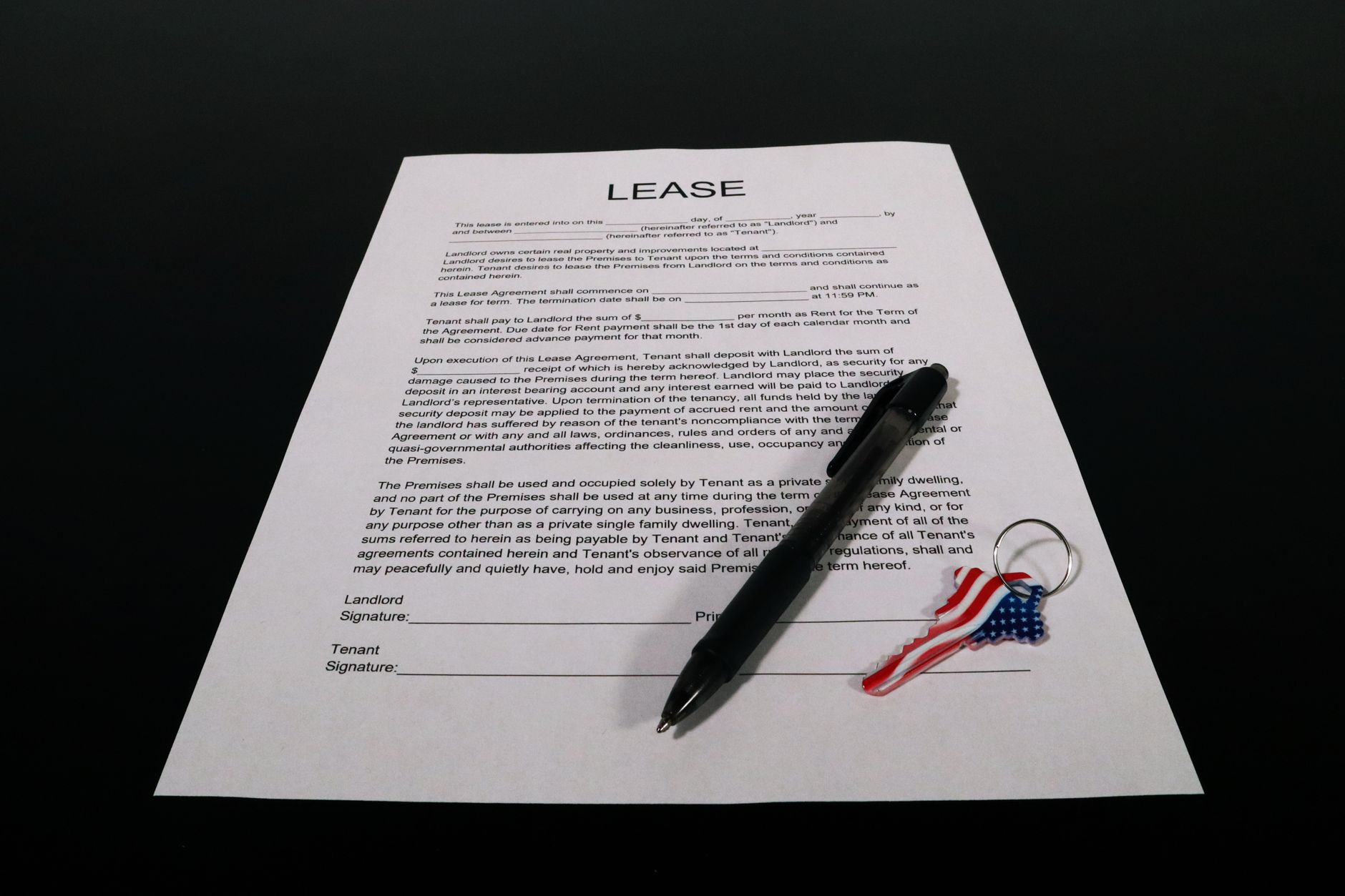 A lease document with a pen and an American flag key on a black surface