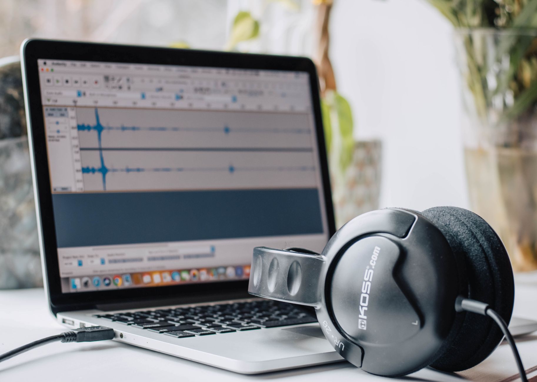 Headphones resting on a laptop showing audio editing software with waveforms