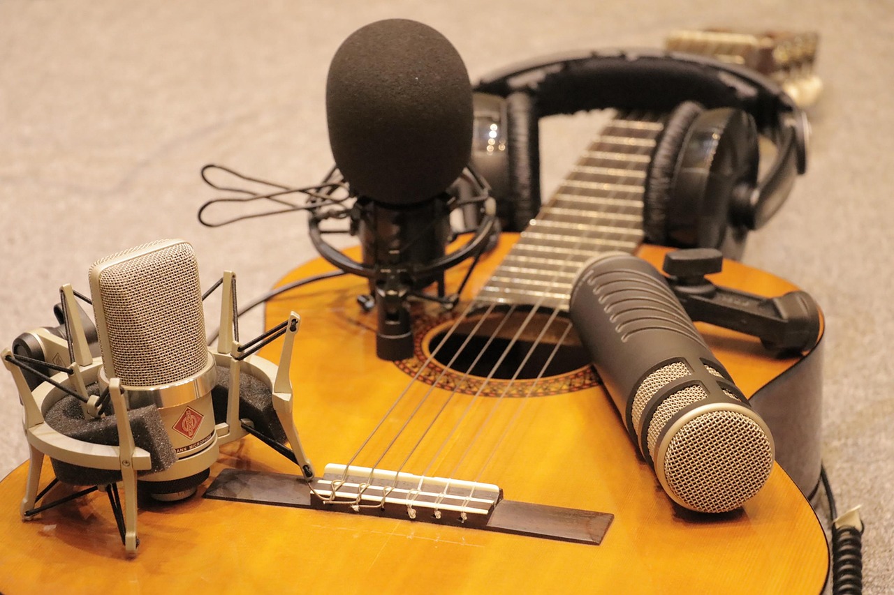 Microphones and headphones rest on an acoustic guitar, ready for audio recording