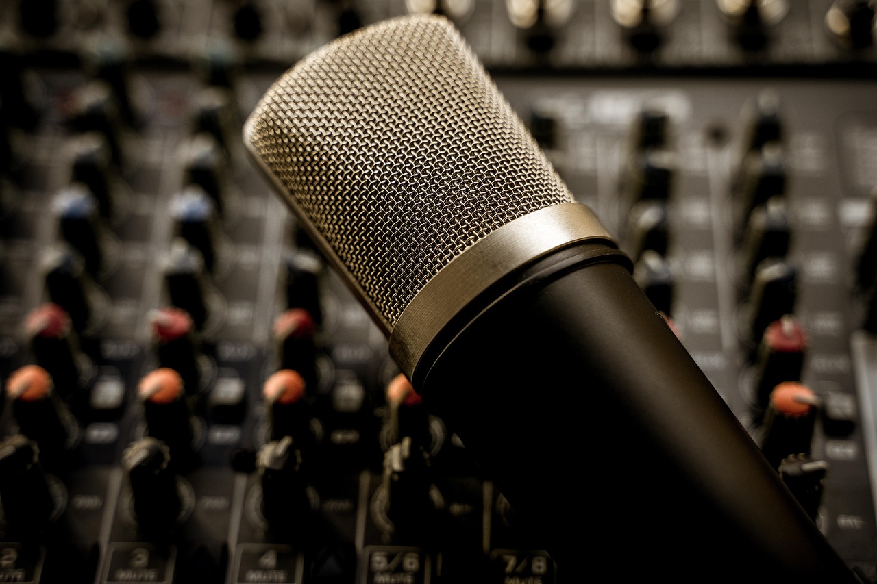 Close-up of a condenser microphone with an audio mixing board in the background