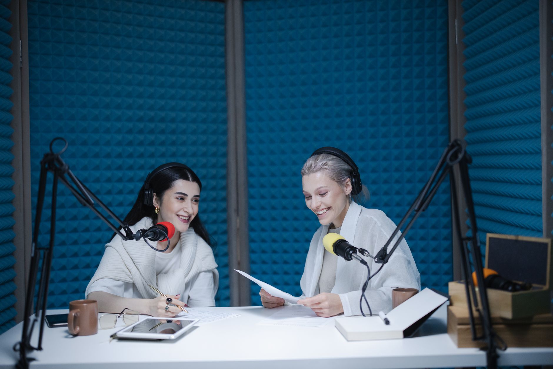 Two smiling women recording a podcast in a studio with microphones and headphones