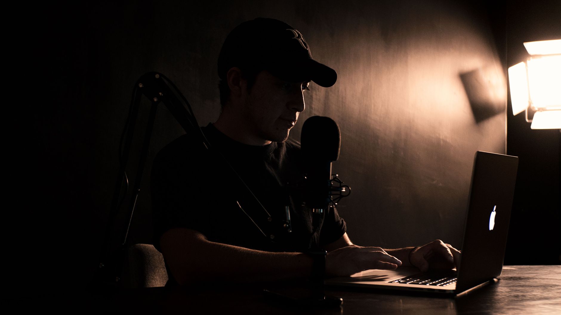 Man in a cap records a podcast on a laptop with a microphone