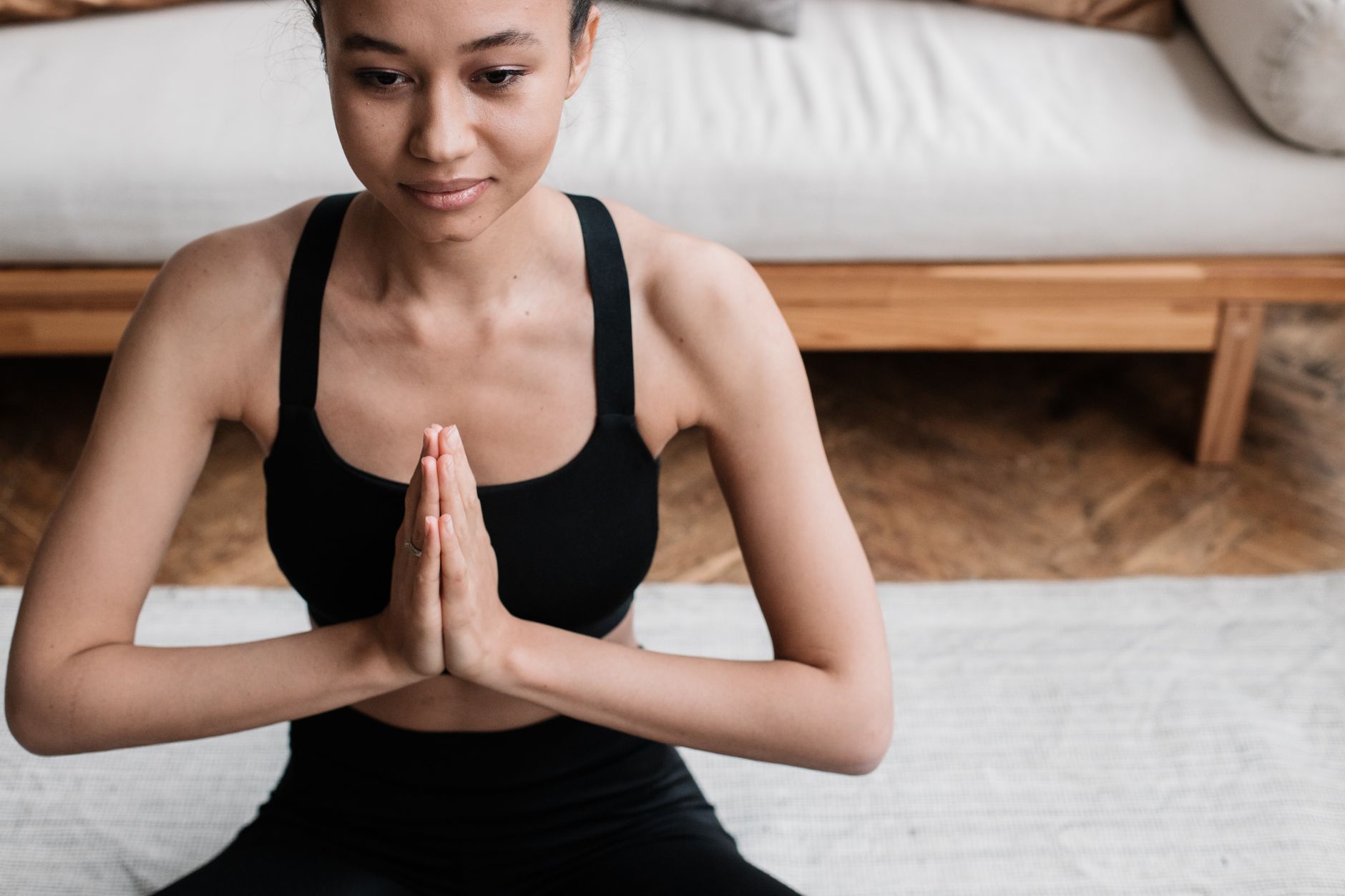 Young woman in black activewear meditating with hands pressed together, practicing wellness rituals