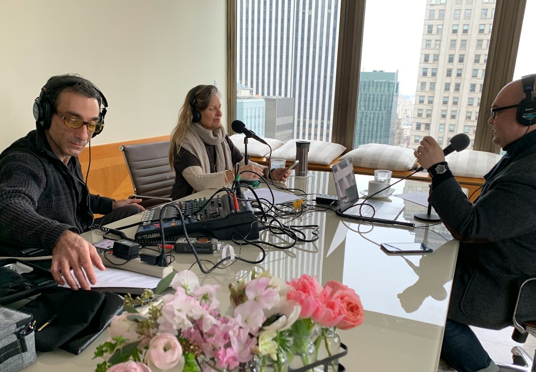 Three people record a podcast with microphones and mixing board in a bright studio