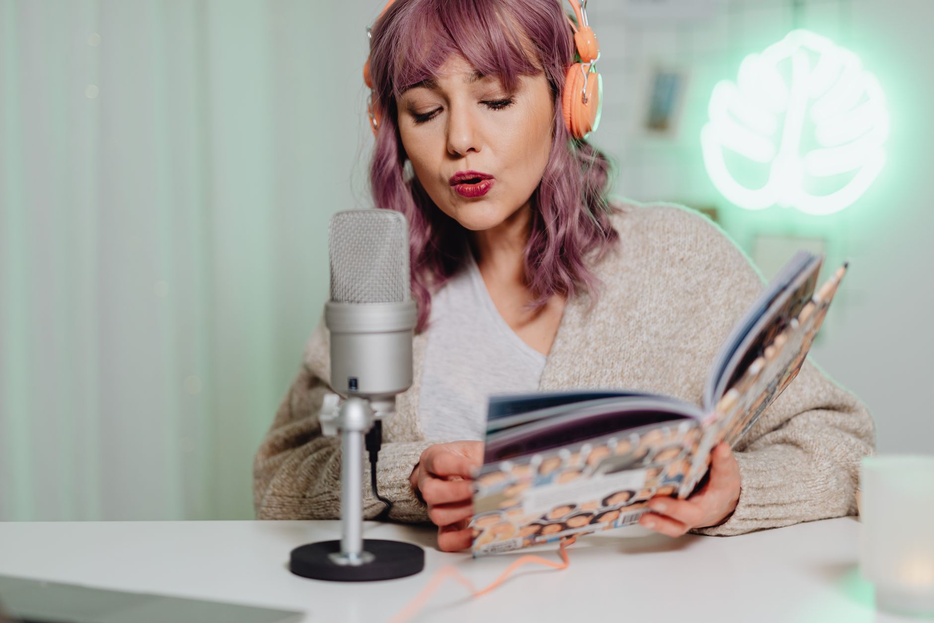 Woman in headphones reading from a book into a podcast microphone in a studio