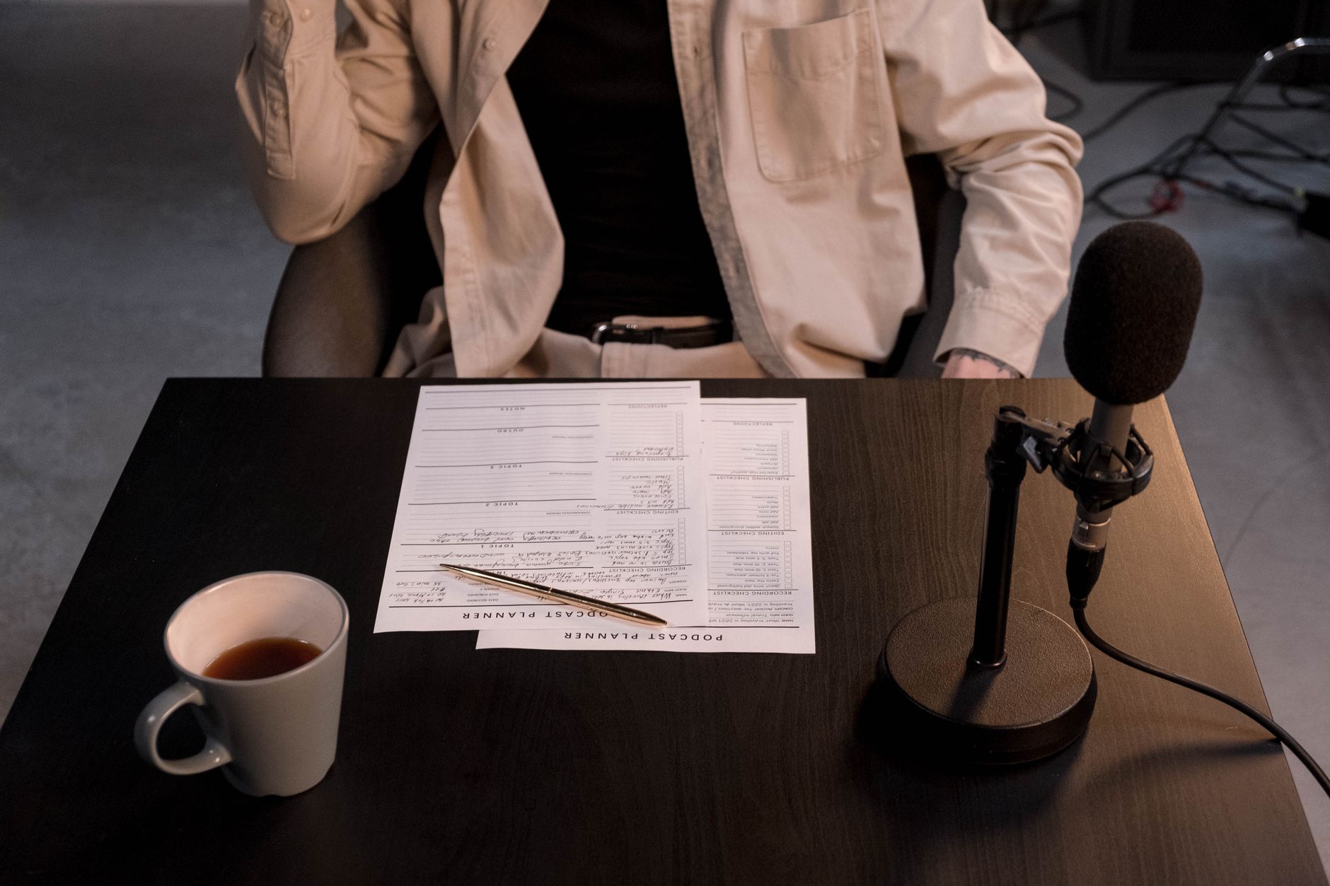 Person planning a podcast, with a microphone, coffee, and a podcast planner