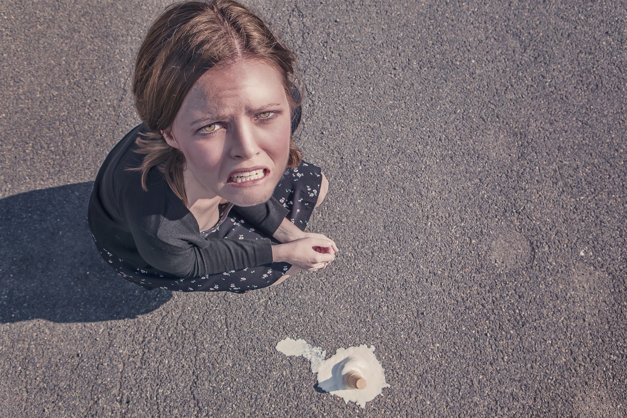 A frustrated woman looks up at a dropped ice cream cone melting on asphalt