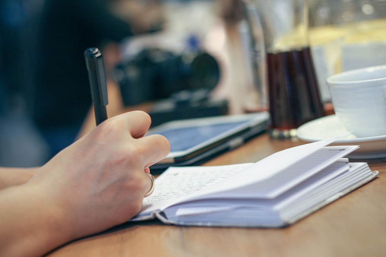 A hand writes with a pen in a notebook, symbolizing human originality and thought