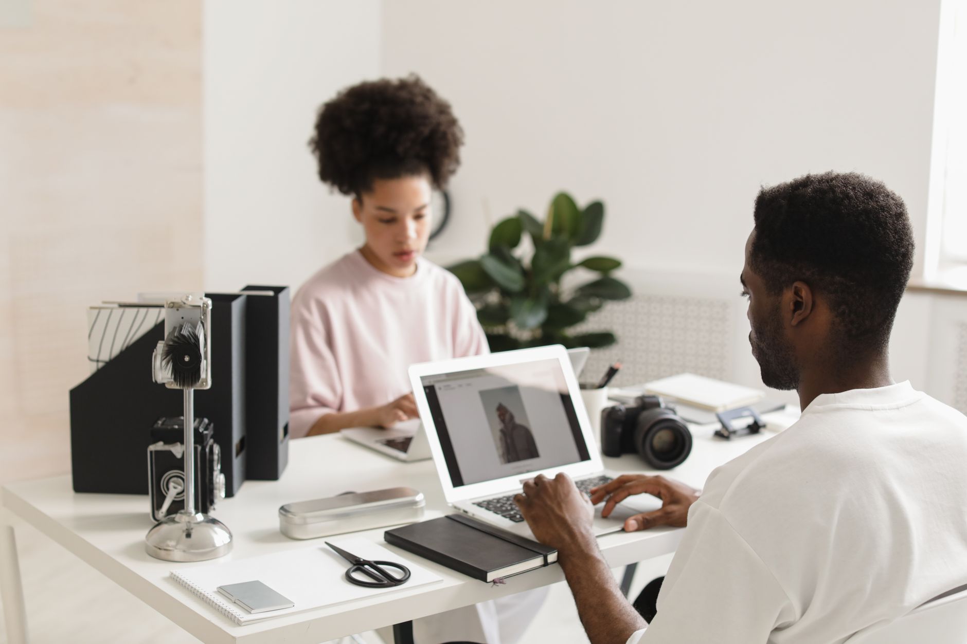 Two people work on laptops at a white desk in a bright office