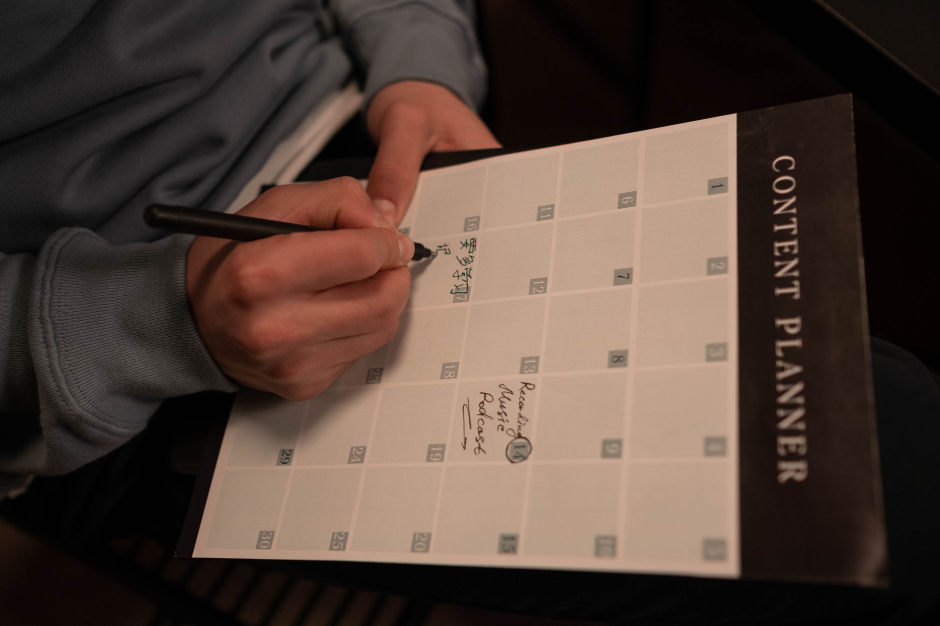 Hands writing a content schedule on a "Content Planner" calendar with a pen
