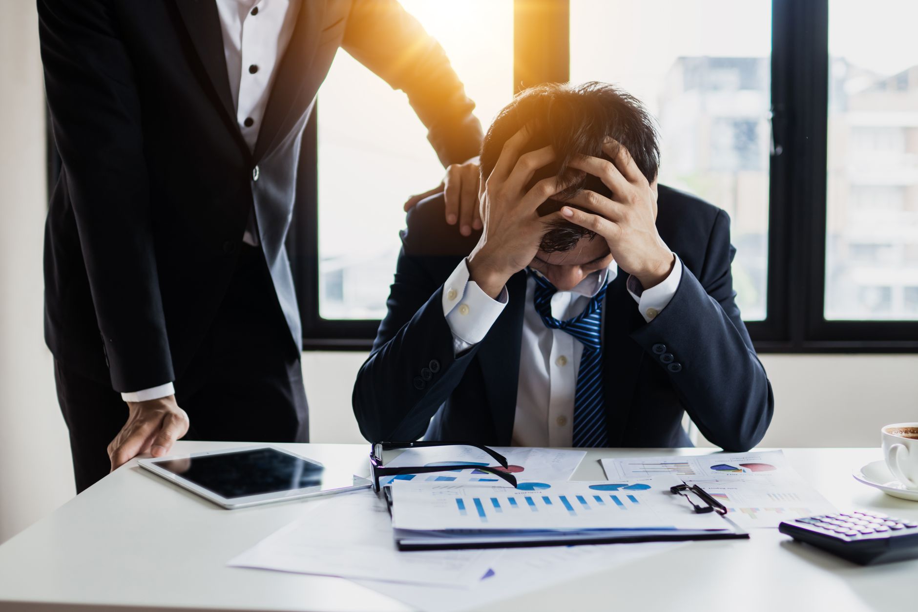 Stressed businessman holding his head, looking at declining traffic charts with support