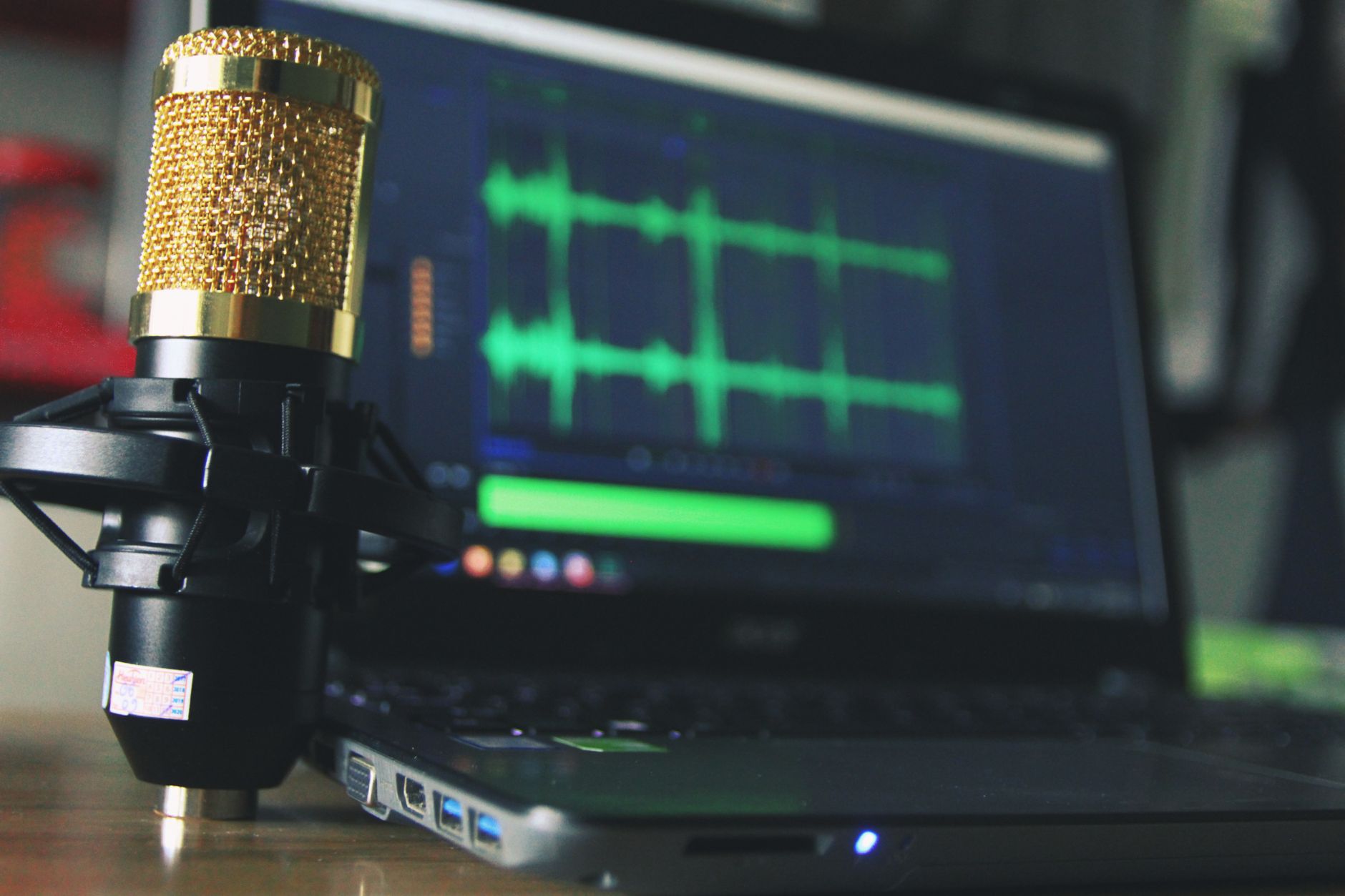 A gold microphone stands beside a laptop displaying green audio waveforms for podcasting
