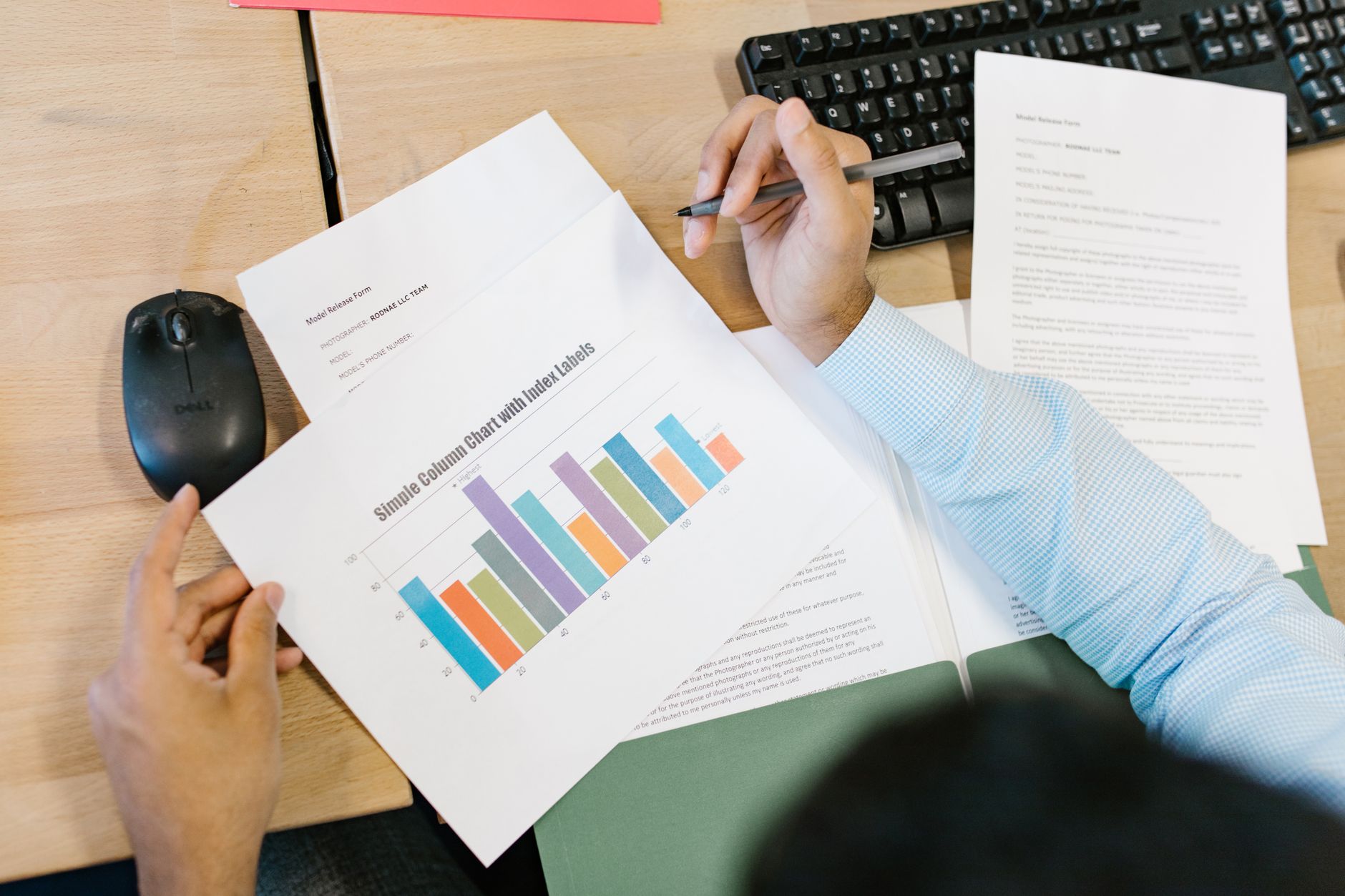 Person reviews a column chart displaying data on paper, alongside other documents on a wooden desk