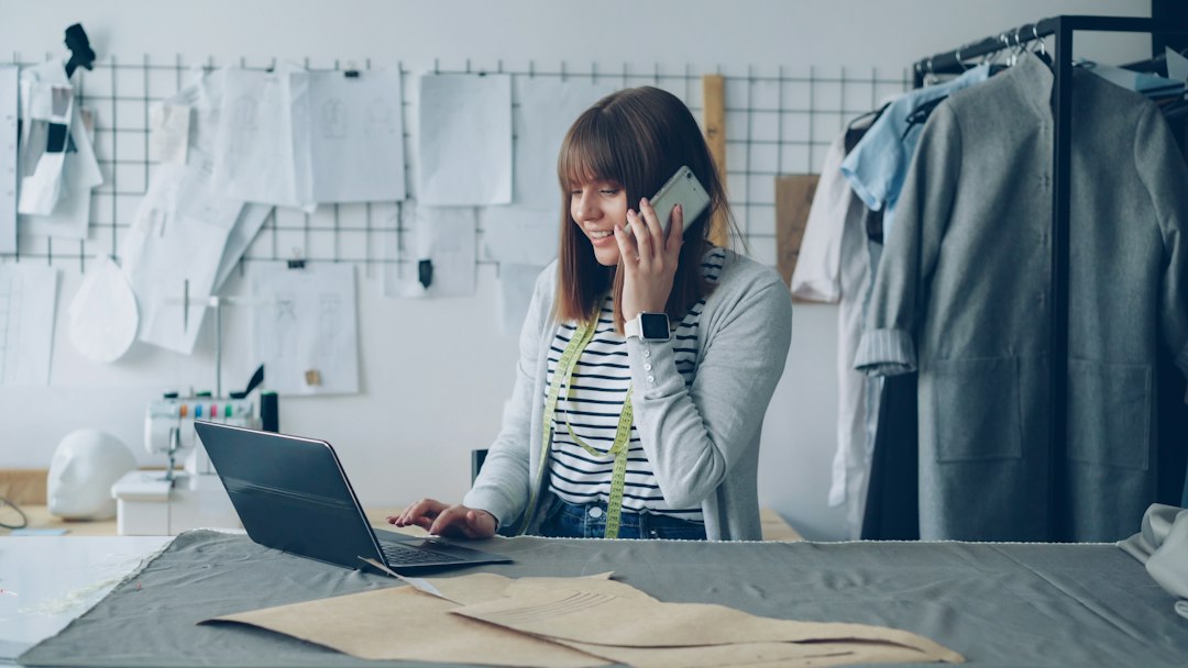 A young fashion designer talks on the phone while working on a laptop