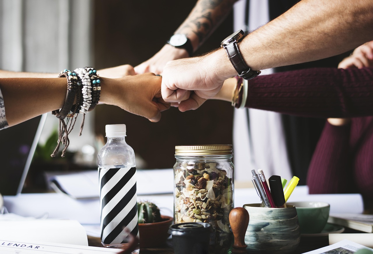 Three people's hands fist-bumping over a desk, symbolizing team collaboration