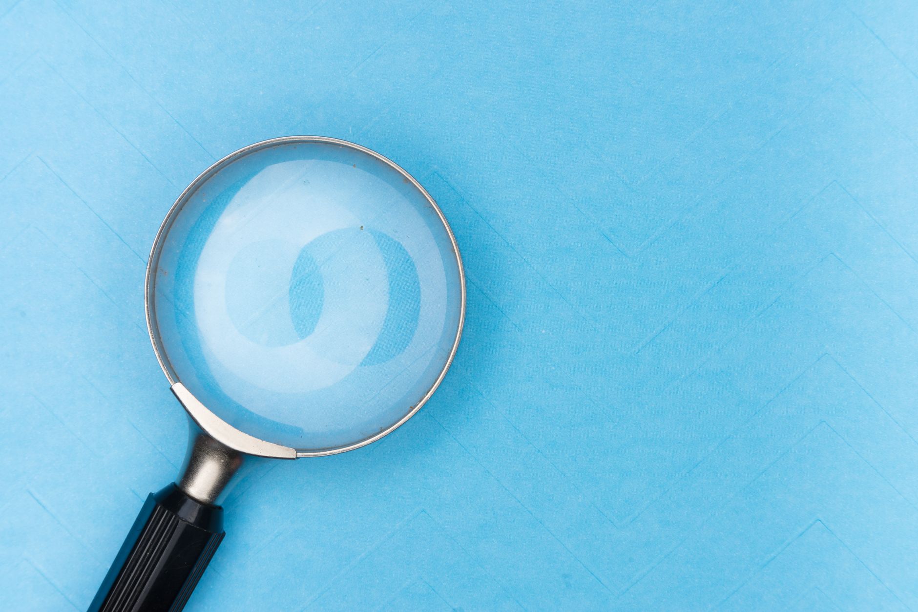 A magnifying glass on a blue textured surface, symbolizing diagnosing indexing issues