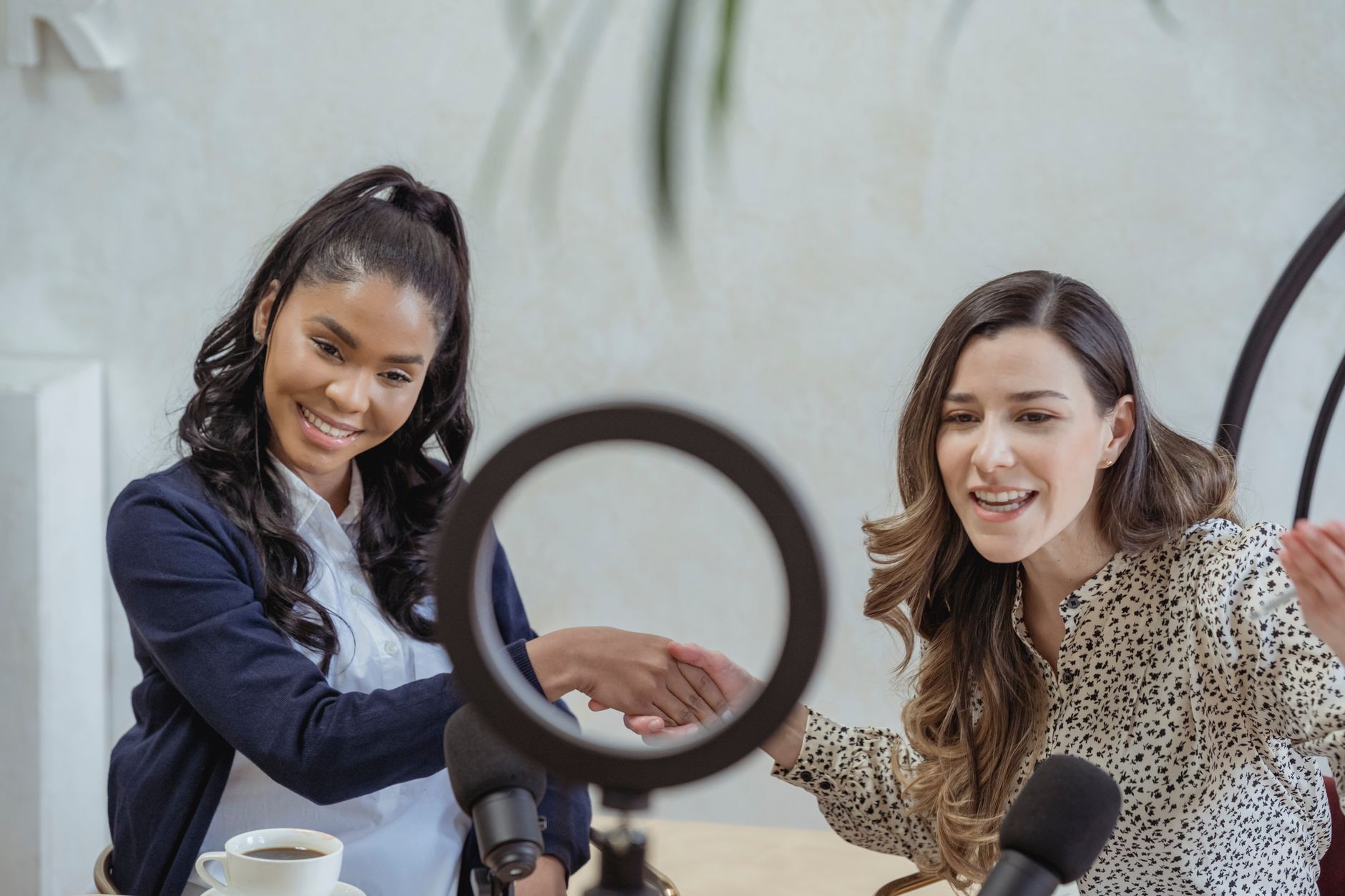 Two women shake hands over a microphone, making a podcast collaboration agreement