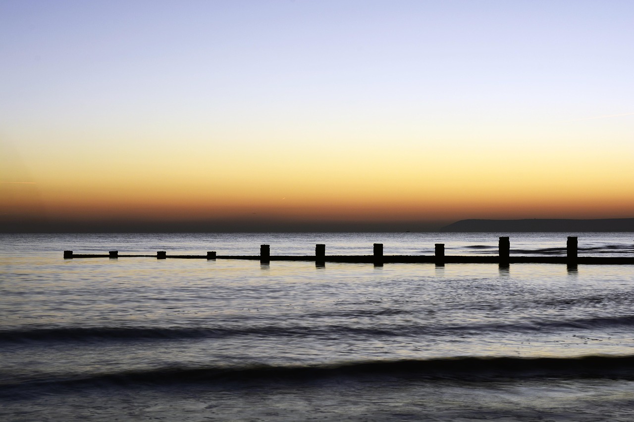 A serene ocean sunset with wooden posts in the water, evoking peaceful body awareness