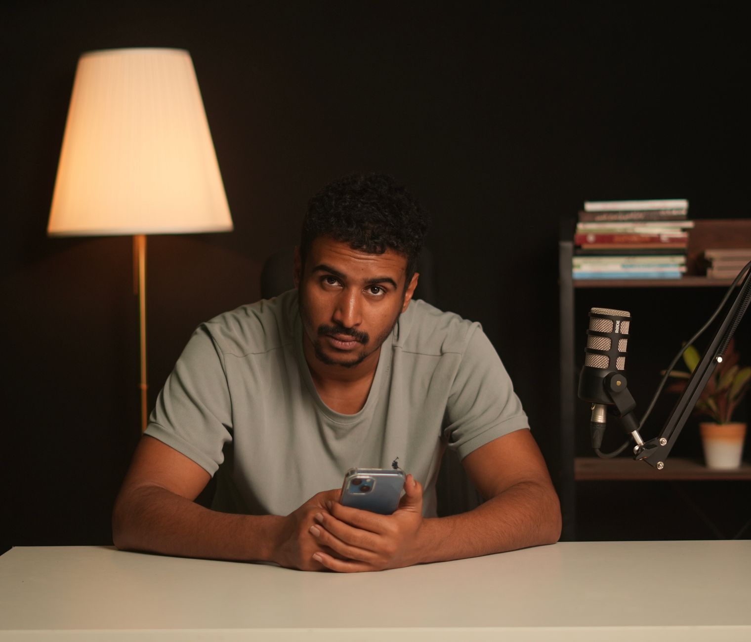 A man sits at a desk holding a smartphone beside a mounted microphone
