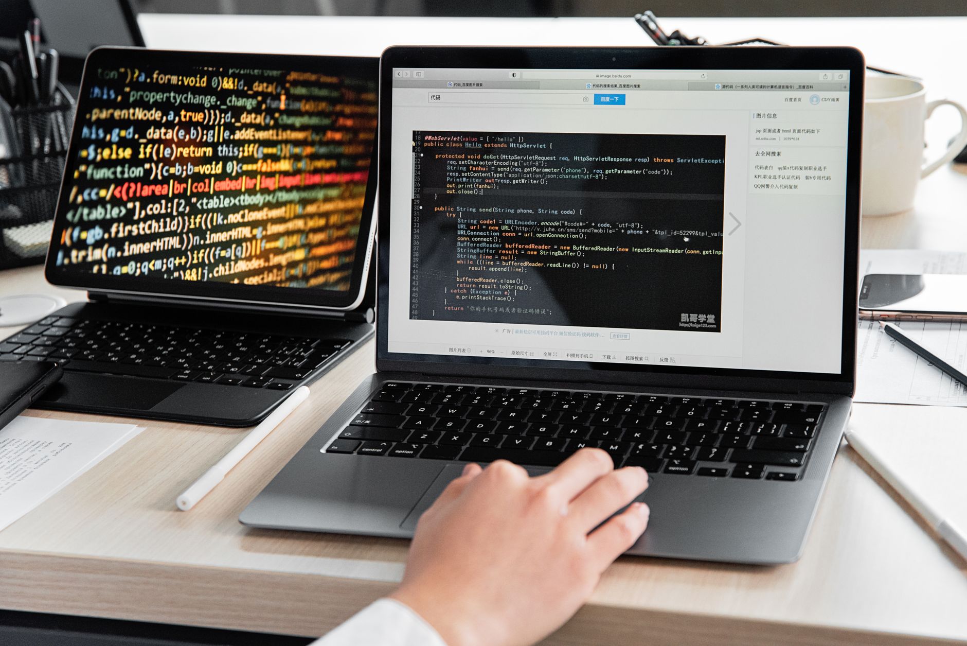 Person typing Java code on a laptop, with another screen displaying colorful code